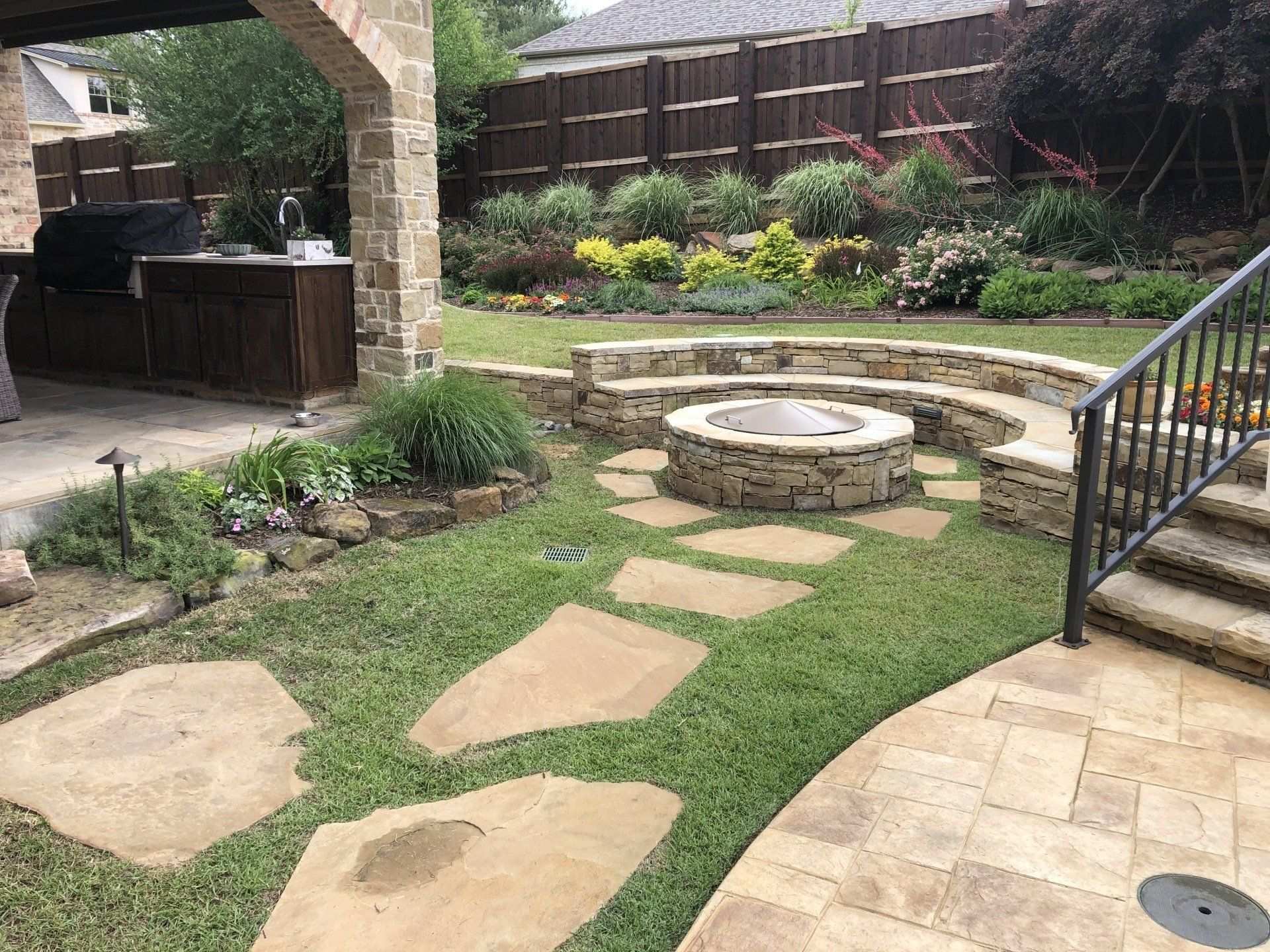 Backyard with flagstone stepping stones, a round stone fire pit and an outdoor kitchen