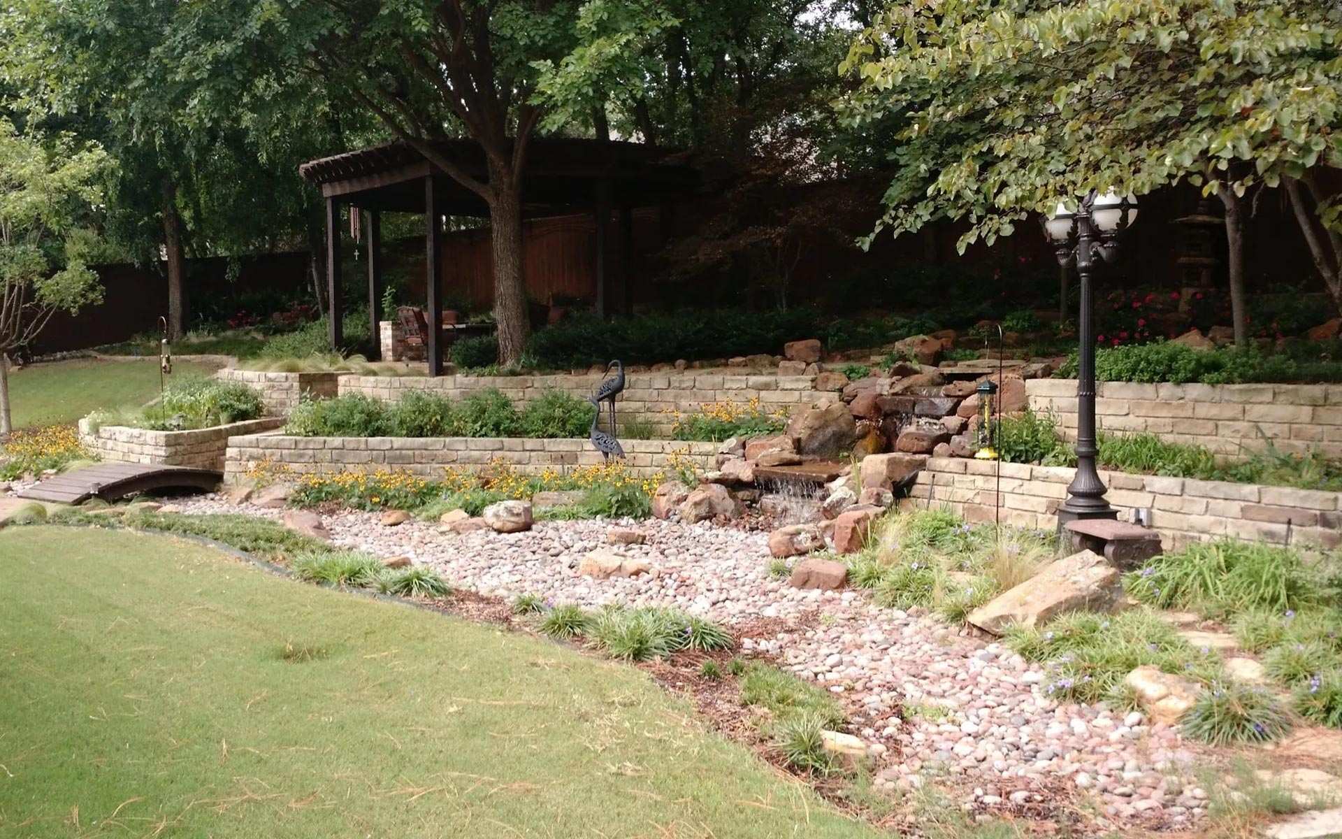 Landscaped bed with a dry creek bed and stone retaining wall beside a lawn